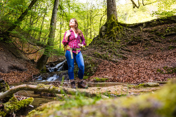 Naklejka na ściany i meble Woman with backpack in a beautiful forest while hiking near a waterfall