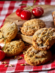 Oatmeal cookies with husk oats and cherry on kitchen cutting board gingham checkered cotton fabric on table in village style for picnic close up. Breakfast for loved one. Bio baking.