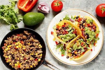 Mexican tacos with fried minced meat with corn and black beans, onions, fresh tomatoes and cilantro are flavored with guacamole sauce. top view.