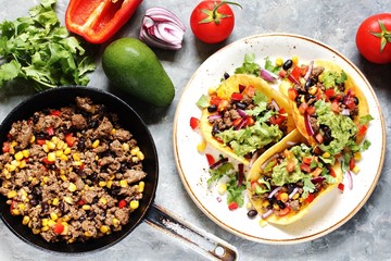 Mexican tacos with fried minced meat with corn and black beans, onions, fresh tomatoes and cilantro are flavored with guacamole sauce. top view.