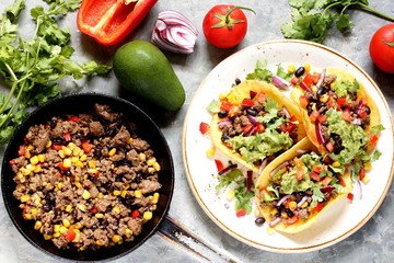 Mexican tacos with fried minced meat with corn and black beans, onions, fresh tomatoes and cilantro are flavored with guacamole sauce. top view.