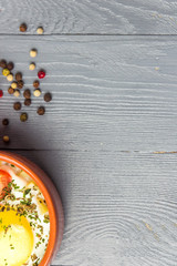 Portioned baked eggs in ceramic cocotte on gray wooden table, breakfast. Top view, copy space for you text.