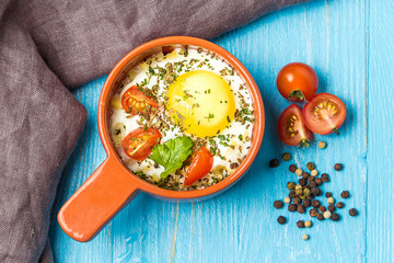Portioned baked eggs in ceramic cocotte on blue wooden table, breakfast. Top view.