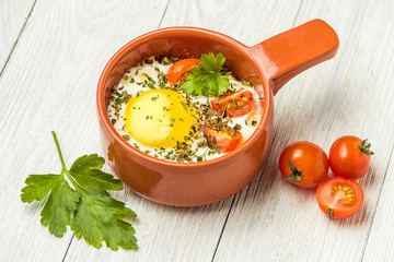 Portioned baked eggs in ceramic cocotte on white wooden table, breakfast.