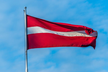 Waving or streaming National flag of Latvia State on background of blue sky