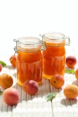 Apricot jam. Orange jam in glass jars set,  ripe apricots on a wooden white table on a light background. High key.Homemade jam.Summer  Canned fruit jam. Healthy vegetarian sweets