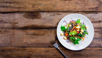 Salad of fresh vegetables in a white dish placed on an old wooden table.top view.