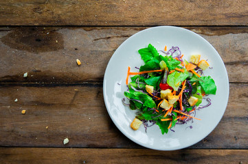 Salad of fresh vegetables in a white dish placed on an old wooden table.top view.
