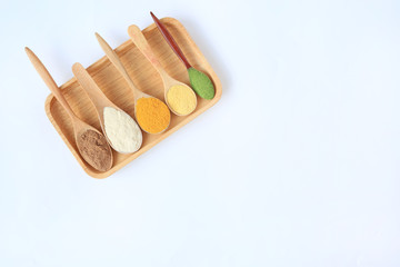 Various colorful powder in different wooden spoons on wood tray with copy space isolated on white background.