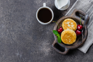 Breakfast Food Delicious Concept. Cottage cheese pancakes, syrniki, curd fritters with cherry on dark concrete table background. Top view, copy space