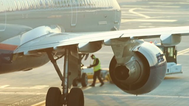 A huge plane standing on the runway on a background of a sunset. A man worker informs that plane is ready