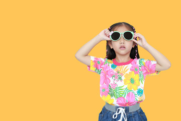 Cute little Asian kid girl wearing a flowers summer dress and sunglasses isolated on yellow background with copy space. Summer and fashion concept.