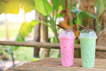Iced green tea matcha latte and Pink strawberry milk of juice for summer put on the bamboo wood table against nature background.