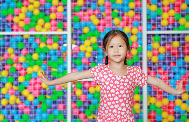 Fototapeta na wymiar Beautiful Asian little girl doing thai style dance open arms expressions against colorful toy ball playground. Expresses pleasant emotions.