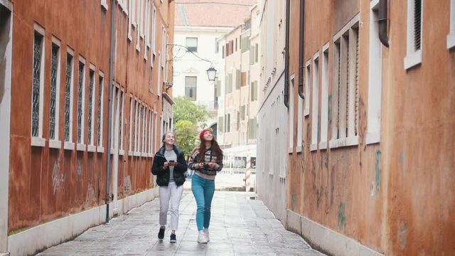 Two young women travelers in warm clothes walking on the narrow streets and talking