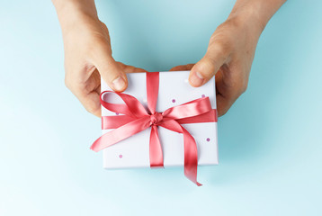Male hands holding gift box with ribbon on blue background, top view