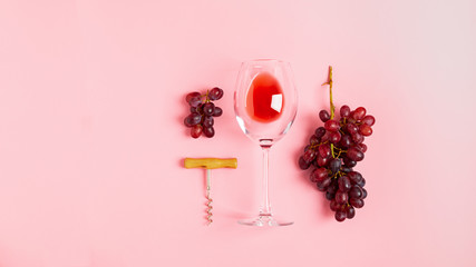 A glass of red wine a bunch of grapes corkscrew on gentle pink background. Minimalism. Top view flat layout. Copy space