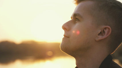 Close up of pensive handsome face young man enjoying nature in sun rays at sunset summer adventure