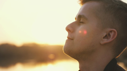 Close up of meditative handsome face young man enjoying nature in sun rays at sunset summer adventure