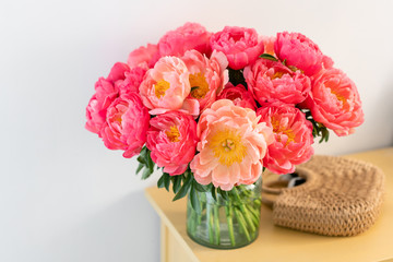 Coral peonies in a glass vase and wicker bag on wooden table.. Beautiful peony flower for catalog or online store. Floral shop concept . Beautiful fresh cut bouquet. Flowers delivery. Copy space