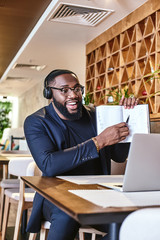 Young businessman with headphones sitting in cafe in front of laptop and networking