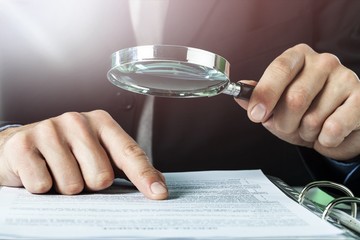 Business analytics and statistics. Businessman with report using a magnifying glass.