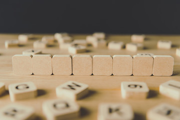 selective focus of eight blank cubes surrounded by blocks with letters on wooden surface isolated on black