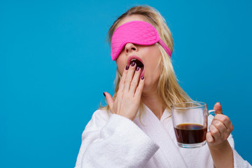 Photo of yawning woman with pink eye patch and cup of coffee