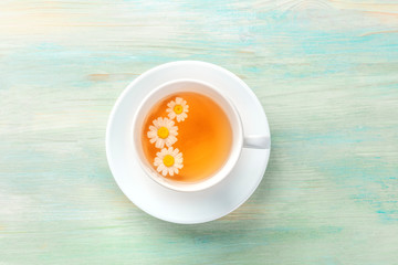 A cup of chamomile tea, shot from the top on a teal blue background with a place for text