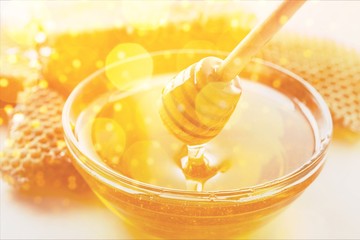 Honey with spoon in glass bowl on glossy background