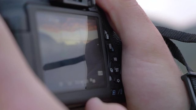 Close-up Of A Young Man Taking A Picture With A Canon Reflex Camera in slowmotion in exterior with cloudy blue sky. it's a wide lens 24mm. We see tactile screen touching it.