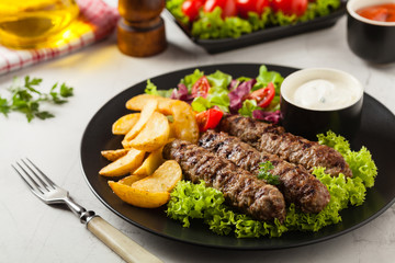 Traditional cevapcici served with baked potatoes. Stone background.
