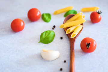 Penne pasta with cherry tomatoes, garlic cloves and basil leaves at table, close-up