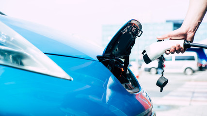 Charging The Electric Car on special station outdoors. Male hand holds adapter
