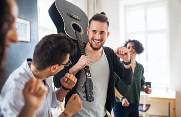 A group of young friends with guitar indoors at home, house sharing concept.