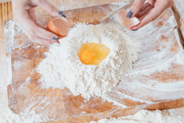 Homemade bakery food and pastry. Culinary course. Closeup of female hands cracked egg straight into flour.