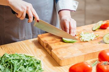 Woman hands cutting chopping cucumber closeup. Organic fresh veggies for healthy balanced vegetarian salad. Dieting.