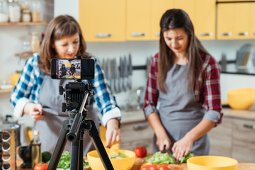 Family hobby. Healthy nutrition. Mother and daughter recording culinary video blog. Ladies making salad with organic vegetables.
