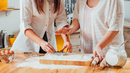 Midsection of two women baking. Mother teaching daughter to cut out flat pastry dough. Home baked foods goods hobby