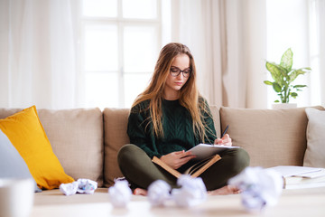 A happy young female student sitting on sofa, studying.