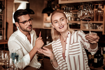 Positive delighted blonde bartender looking at wineglass