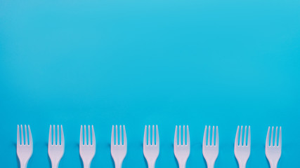 Air pollution. Plastic littering. Ecology problem. White disposable fork row at bottom of sky blue background. Copy space.