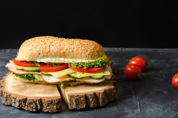 Delicious sandwiches with ham, cheese, tomatoes and salad over a wooden board on black background. Space for text