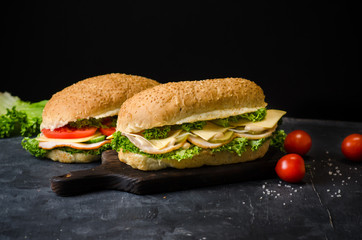 Two delicious sandwiches with ham, cheese, tomatoes, salty cucumber and salad over a wooden board on black background. Space for text