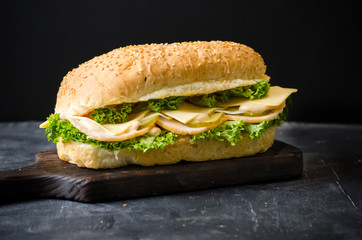 Delicious sandwiches with ham, cheese, salty cucumber and salad over a wooden board on black background.