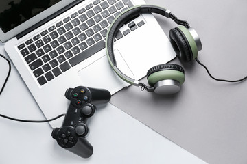 Laptop, game pad and headphones on grey background