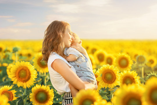 Beautiful woman with her little son in sunflower field on summer day