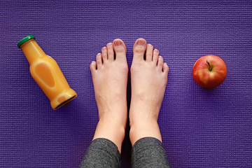 Naklejka premium Legs of sporty woman with apple and bottle of juice on yoga mat