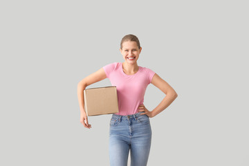 Young woman with cardboard box on light background