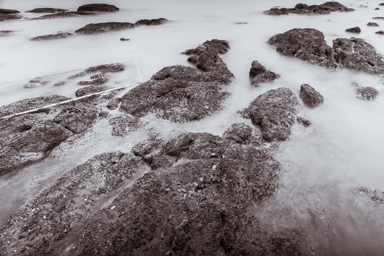 Photo Black and White of Long Exposure Photography Waves on stone beach waters edge abstract sea background.Thailand.